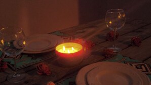 Una mesa de madera adornada con platos, vasos y una vela encendida, rodeada de rosas artificiales.