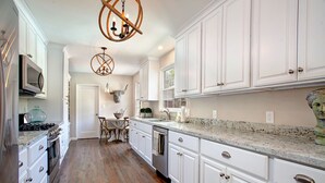 Una cocina con gabinetes blancos, encimera de granito, electrodomésticos de acero inoxidable y suelo de madera.