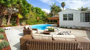 Un patio trasero con piscina, muebles de mimbre y una pequeña casa blanca.