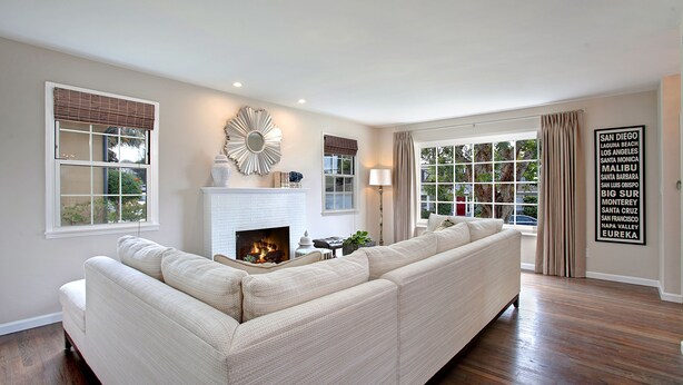 Una sala de estar con un amplio sofá seccional beige, una chimenea y vistas al exterior a través de grandes ventanales.