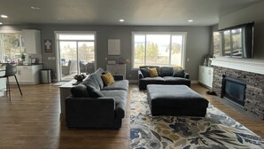 A spacious living area with a fireplace, a kitchen in the background, and large windows providing natural light. - Beautiful 3 bed+den, 3bath huge home on the Spokane River and Centennial Trail (Spokane Valley)