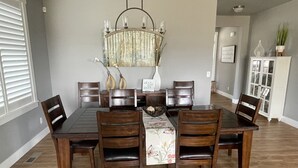 A dining room with a rectangular table surrounded by six wooden chairs, a chandelier above, and a cabinet with decorative items to the side. - Beautiful 3 bed+den, 3bath huge home on the Spokane River and Centennial Trail (Spokane Valley)