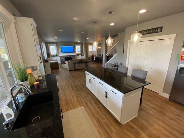 A modern kitchen with a black countertop, white cabinets, and a built-in stove. There is a dining area with a table and chairs, and a staircase leading to another level. - Beautiful 3 bed+den, 3bath huge home on the Spokane River and Centennial Trail (Spokane Valley)