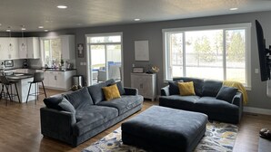 A modern living room with grey sofas, a coffee table, and a kitchen in the background. - Beautiful 3 bed+den, 3bath huge home on the Spokane River and Centennial Trail (Spokane Valley)