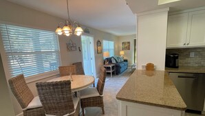 A kitchen with a dining area, featuring a granite countertop, wicker chairs, and a hanging light fixture. - 2 Bedroom / 2 Bath Ground Level With a Heated Pool (Holmes Beach)