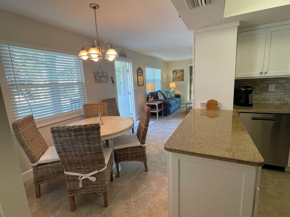 A kitchen with a dining area, featuring a granite countertop, wicker chairs, and a hanging light fixture.
