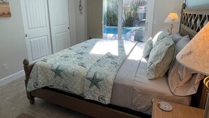 A bedroom with a bed, a nightstand, a lamp, and a view of a pool through a glass door. - 2 Bedroom / 2 Bath Ground Level With a Heated Pool (Holmes Beach)