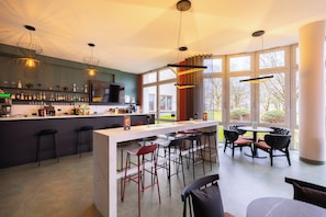 Un área de bar moderna con mostrador, taburetes y un espacio de estar con sillas y una mesa.