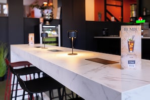 A bar area with a marble countertop, black chairs, and a menu stand for Bumbu craft rum.