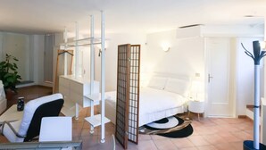 A modern hotel room with a bed, bedside table, lamp, and a desk with a chair.