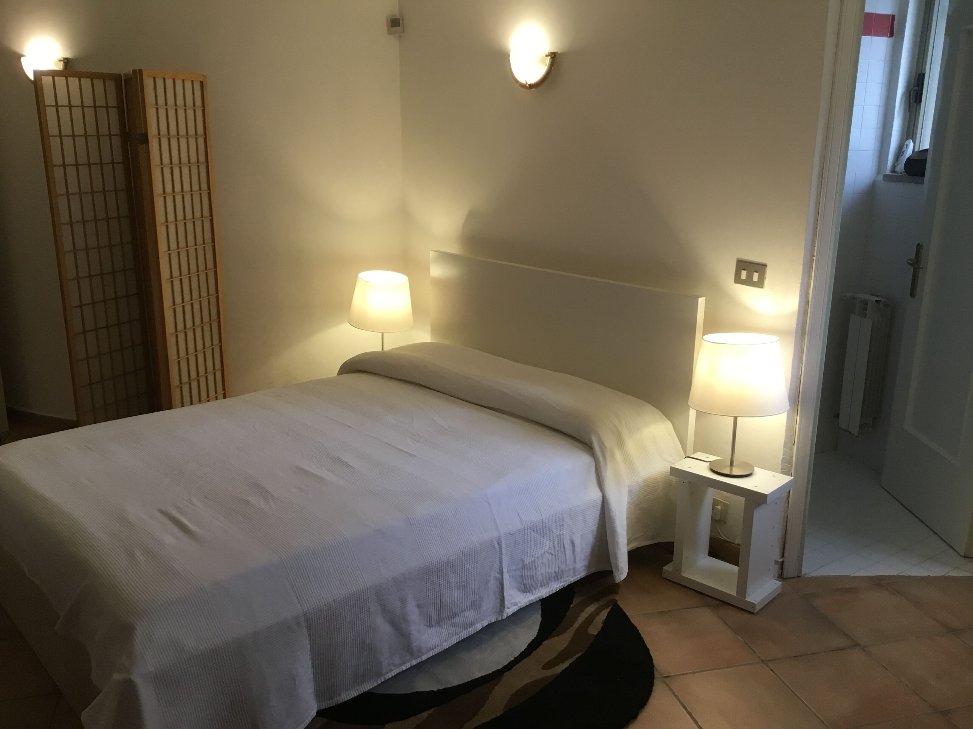 Un lit bien fait, avec du linge de lit blanc, deux lampes de chevet et une cloison en bois d’un côté.