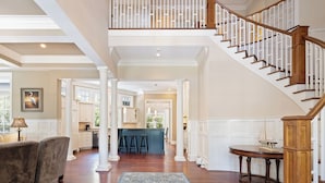 A spacious interior with a wooden staircase, a kitchen area, and a seating area with a blue rug.