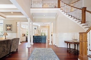 Un intérieur spacieux avec un escalier en bois, un coin cuisine et un espace salon agrémenté d’un tapis bleu.