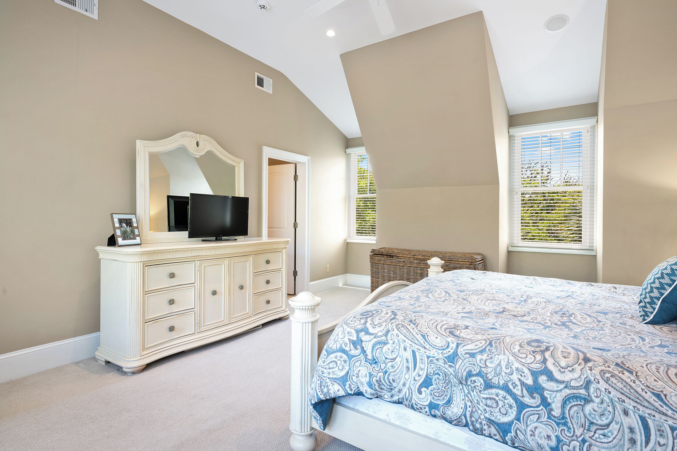 A bedroom with a bed, dresser, television, and a window with blinds.