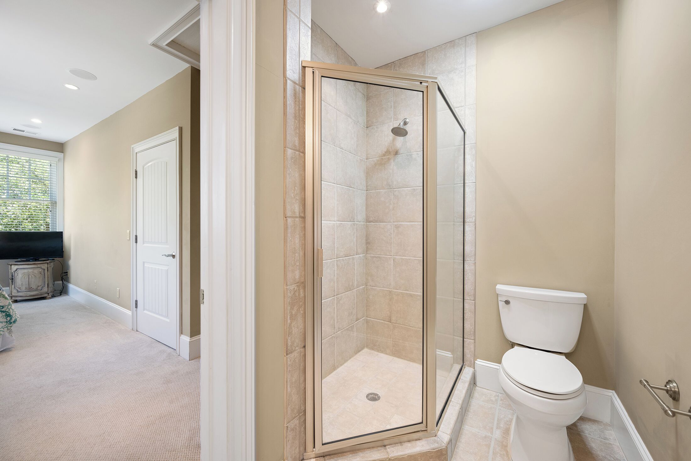 A bathroom with a glass-enclosed shower, a toilet, and a door leading to another room.