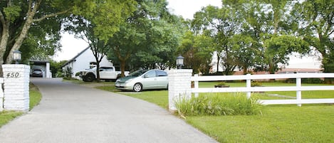 A driveway leading to a house with a number 450 sign, a white fence, and a parked car.