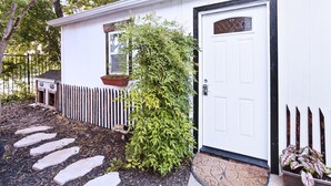 Un bâtiment blanc avec une porte à encadrement noir, une petite fenêtre et un pot de fleurs placé à côté.
