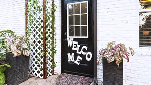 A black door with a welcome sign, white brick walls, and potted plants. - Guest Efficiency at Gold Farm (McKinney)