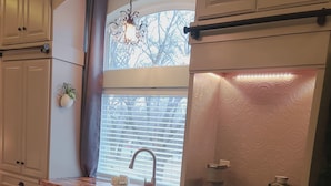 A kitchen with white cabinets, a window with blinds, a sink, and a microwave. - Guest Efficiency at Gold Farm (McKinney)