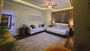 A modern bedroom with a ceiling fan, a bed with a headboard, a bedside table with a lamp, and a small side table with a plant. - Guest Efficiency at Gold Farm (McKinney)