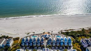 Luchtfoto van een strandhotel met meerdere gebouwen met blauwe daken, een zandstrand en een helder uitzicht op de oceaan.