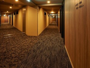 Pasillo de hotel con pisos alfombrados y paredes de madera, con puertas que tienen números de habitación.