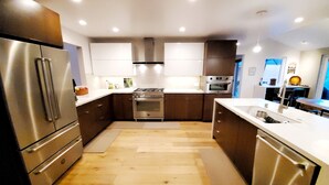 A modern kitchen with stainless steel appliances, wooden flooring, and white cabinetry. - Stunning new home on creek, with spa pool, 5min walk to wineries & restaurants (Glen Ellen)