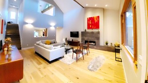 A modern living room with a white sofa, wooden flooring, a fireplace, and a large window. - Stunning new home on creek, with spa pool, 5min walk to wineries & restaurants (Glen Ellen)