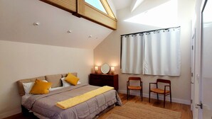 A bedroom with a sloped ceiling, a bed with a headboard, two chairs, a rug, and a window with curtains. - Stunning new home on creek, with spa pool, 5min walk to wineries & restaurants (Glen Ellen)