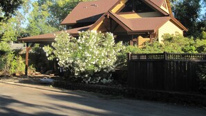 A two-story house with a brown roof, a covered porch, and a stone wall. - Stunning new home on creek, with spa pool, 5min walk to wineries & restaurants (Glen Ellen)