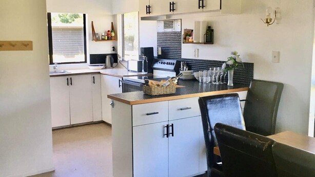 Een moderne keuken met witte kasten, een centraal eiland met een spoelbak en een eethoek met een tafel en stoelen.