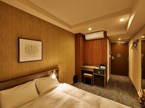 Habitación de hotel con cama, escritorio y silla. Se observa un cuadro enmarcado en la pared y un equipo de aire acondicionado sobre el escritorio.
