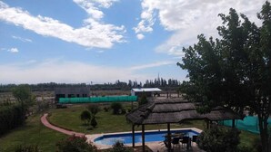 A pool area with a thatched-roof gazebo, a red pathway, and a view of distant buildings. - House for rent for this summer 2021 in San Rafael Mendoza (San Rafael)