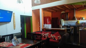 A cozy living room with a sofa, a dining table, and a television. There is a kitchen area with a stove and cabinets. - House for rent for this summer 2021 in San Rafael Mendoza (San Rafael)