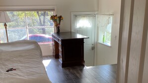 Een slaapkamer met een bed, een dressoir en een raam met uitzicht op bomen en een geparkeerde auto.