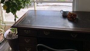Een kamer met een groot raam, een bureau met een waterkoker en een kaart, en een potplant.