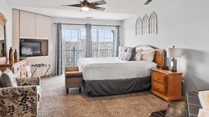 Ein Schlafzimmer mit Bett, Fernseher, Deckenventilator und Blick auf die Stadt durch große Fenster.