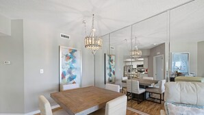 A modern dining area with a wooden table, white chairs, and a chandelier. - The Palms 513 by Liquid Life (Orange Beach)
