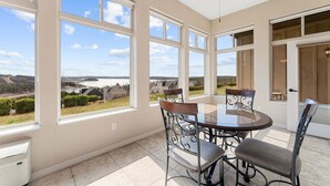 A room with large windows, a ceiling fan, a dining table with chairs, and a view of a lake and houses. - Luxury Walk-In Condo • 2 King Suites • Sunroom + Patio • Near Branson Fun! (Branson)