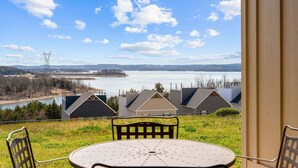 A view from a balcony with a table and chairs, overlooking a body of water, houses, and a distant power line tower. - Luxury Walk-In Condo • 2 King Suites • Sunroom + Patio • Near Branson Fun! (Branson)