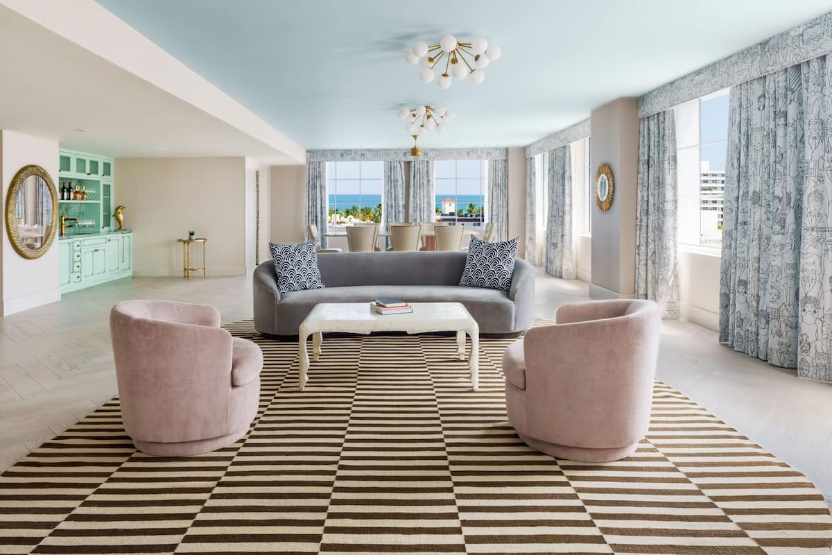 A spacious living room with a grey sofa, two armchairs, a patterned rug, and a view of the sea through large windows.