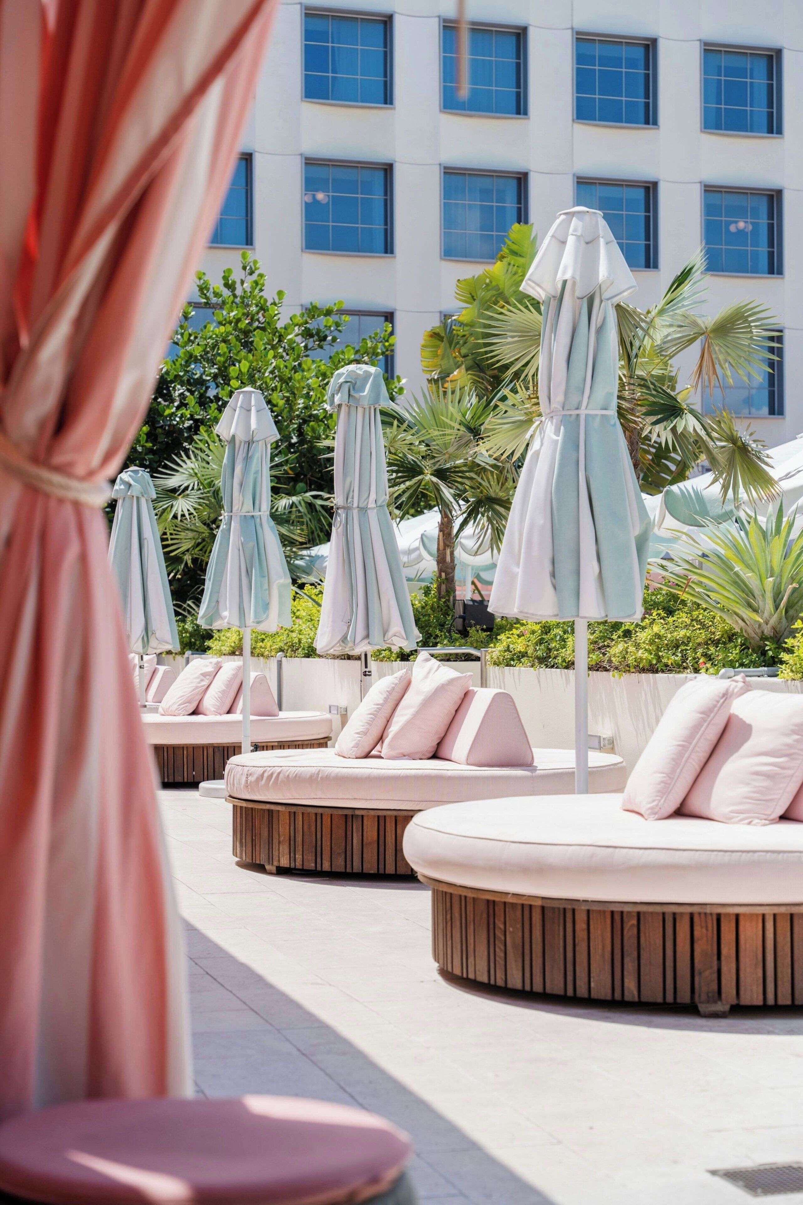 A poolside area with lounge chairs and umbrellas, a building with multiple windows in the background, and lush greenery.