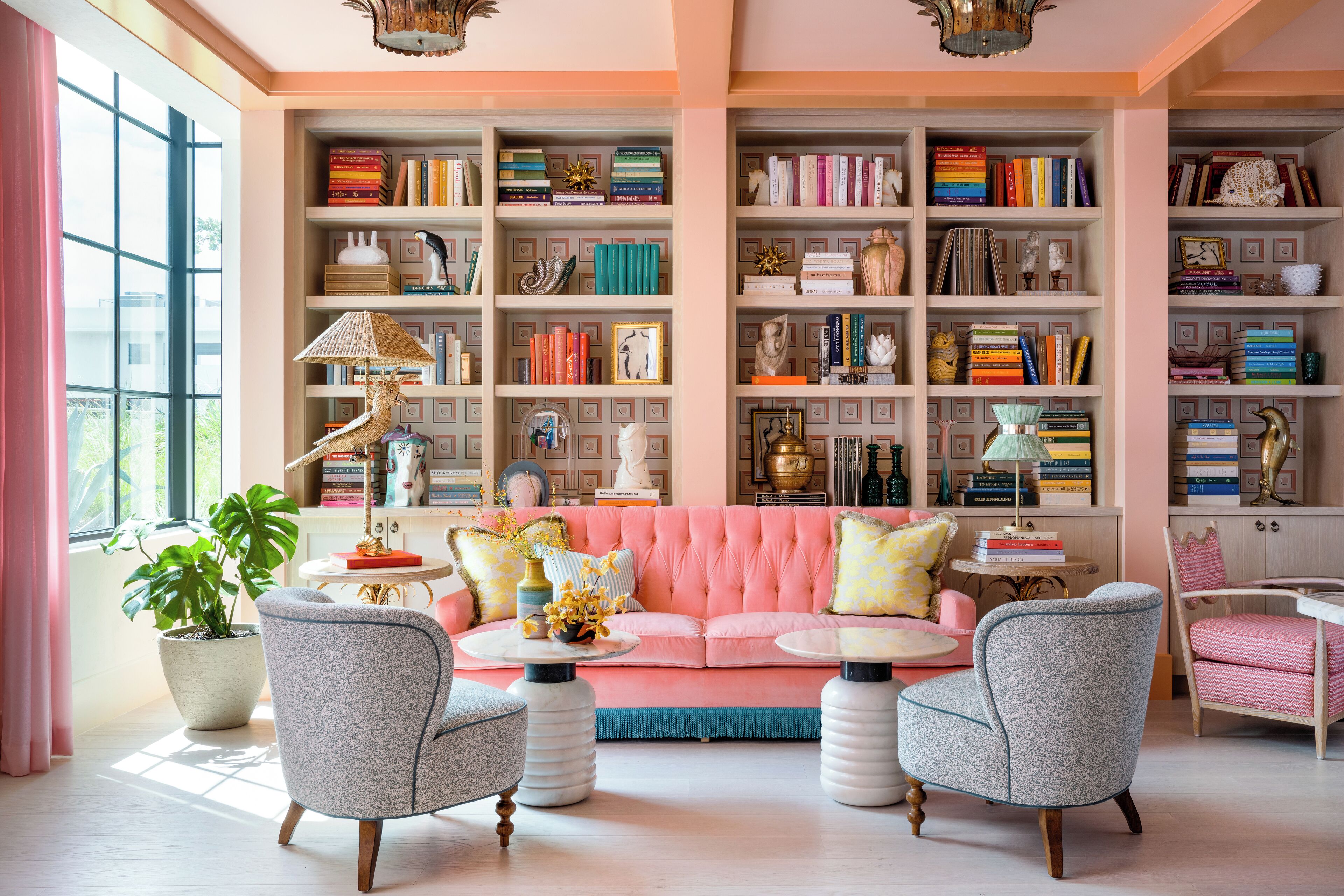 Un salon chaleureux avec un canapé rose, deux fauteuils, une bibliothèque remplie de livres et une plante en pot.