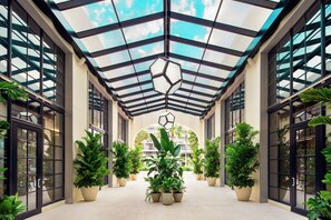 Un atrium abrité avec un plafond en verre, de grandes plantes en pot et un luminaire aux formes géométriques.