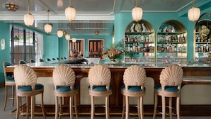 A bar area with a teal color scheme, wooden bar stools with blue cushions, and a variety of bottles and glasses on shelves. - the goodtime hotel, Miami Beach, a Tribute Portfolio Hotel (Miami Beach)