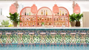 A bar area with a tiled floor, multiple stools, and a decorative partition with bottles. - the goodtime hotel, Miami Beach, a Tribute Portfolio Hotel (Miami Beach)
