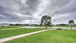 Ein Golfplatz mit einem großen Baum, einem Teich und bewölktem Himmel.