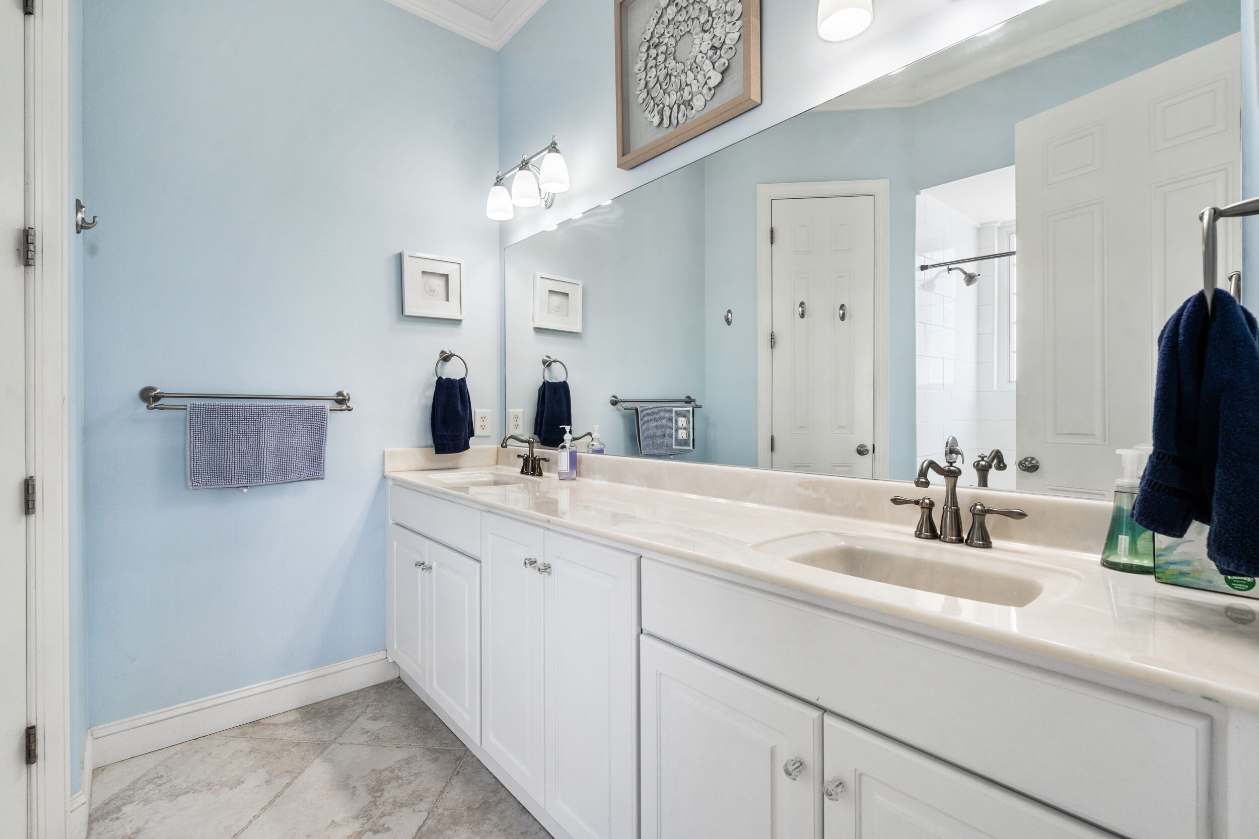 A bathroom with a double sink, white cabinets, a large mirror, and a towel rack.