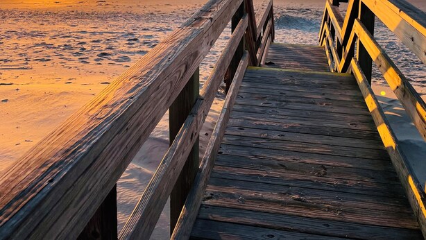 A wooden boardwalk leading to a beach with a sunset in the background.