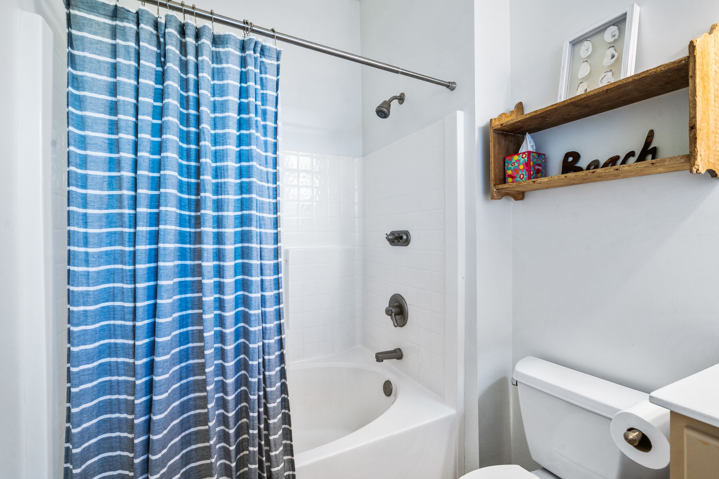 Une salle de bain avec un rideau de douche, une baignoire, des toilettes et une étagère sur laquelle est posé un objet décoratif.